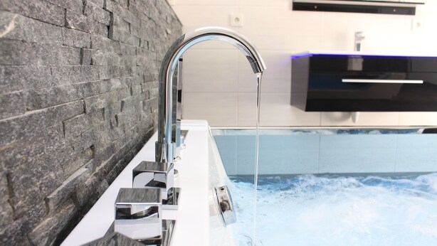 A modern bathroom with a stone wall, a chrome faucet, and a bathtub filled with water.