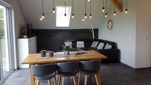 A modern kitchen with a wooden table and chairs, a black sofa, and pendant lights.