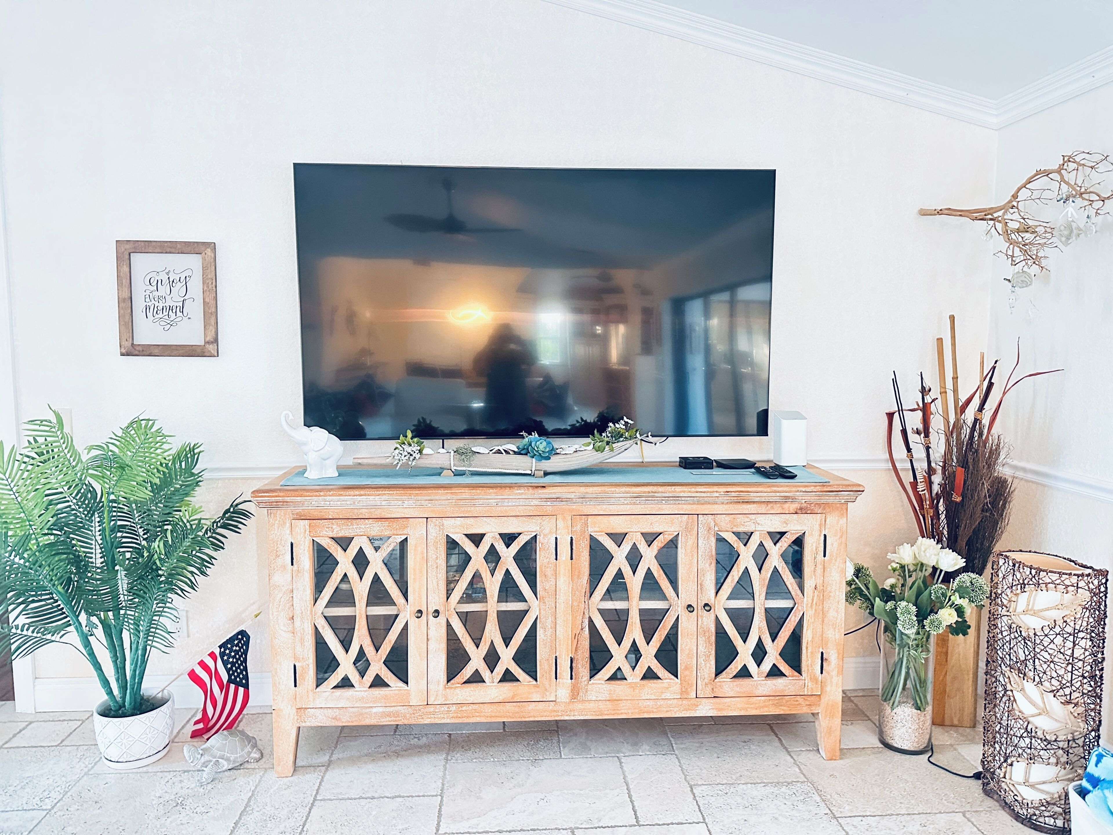 Un salon comprenant un meuble en bois, un téléviseur et divers objets décoratifs, notamment des plantes et un panneau encadré.