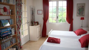 Une chambre avec deux lits, une bibliothèque, une fenêtre avec des rideaux et une porte.