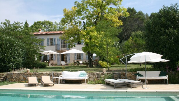 Un espace piscine avec des chaises longues et des parasols, un mur en pierre et, au fond, un bâtiment avec un toit recouvert de tuiles.