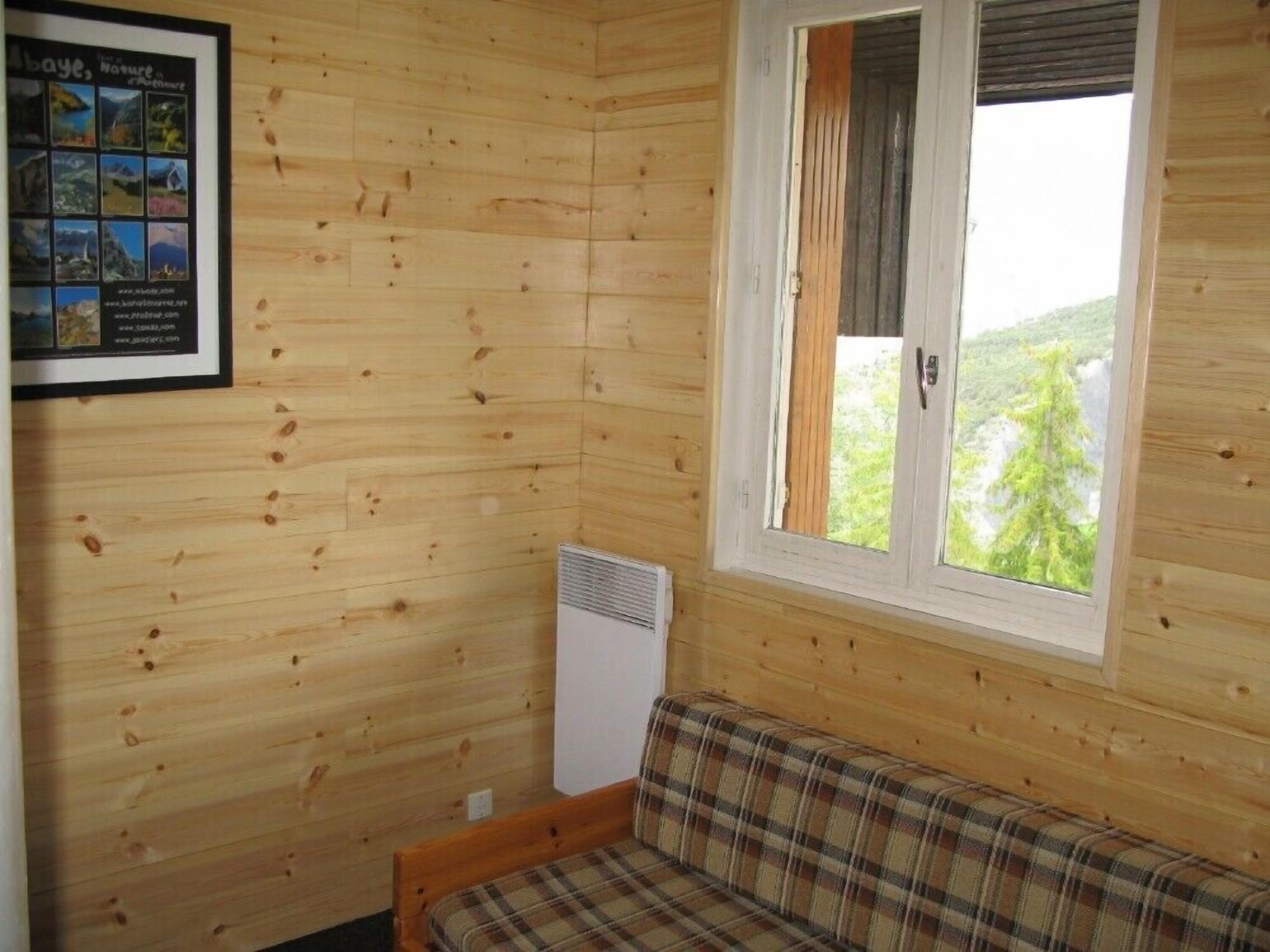 Une pièce de chalet en bois avec un canapé à carreaux, un collage de photos encadrées et une fenêtre donnant sur un paysage verdoyant.