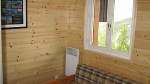 Een houten kamer met een ruitjesbank, een lijst met foto’s en een raam met uitzicht op groen.