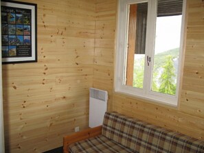 Une pièce de chalet en bois avec un canapé à carreaux, un collage de photos encadrées et une fenêtre donnant sur un paysage verdoyant.