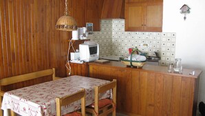 Een kleine keuken met houten kastjes, een magnetron en een tafel met een tafelkleed.