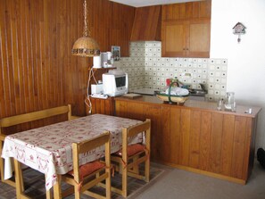 Une petite cuisine avec des meubles en bois, un four à micro-ondes et une table recouverte d’une nappe.