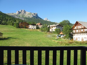 Un village rural avec des maisons traditionnelles en bois, un champ verdoyant et une montagne en arrière-plan.