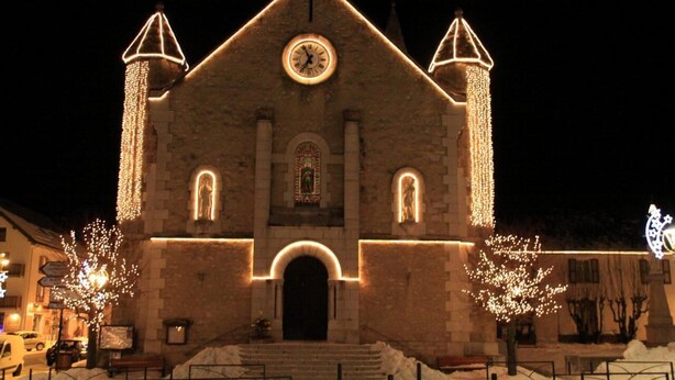 Una iglesia con un reloj, iluminada por luces, y el suelo cubierto de nieve.