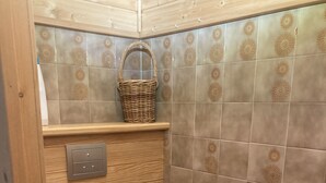 Un baño pequeño con inodoro, una estantería de madera con una cesta y baldosas estampadas.