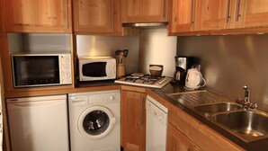 Una cocina compacta con armarios de madera, microondas, lavadora, lavavajillas y un lavabo.