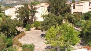 Eine Villa mit einem gepflasterten Innenhof, umgeben von üppiger Vegetation und Blick auf die Berge.