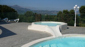 Ein Poolbereich mit Holzterrasse, zwei Whirlpools und Blick auf Berge und ein Gewässer.