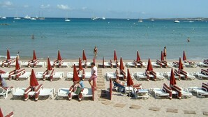 Ein Strand mit Liegestühlen und Sonnenschirmen, klares blaues Meer und Boote in der Ferne.