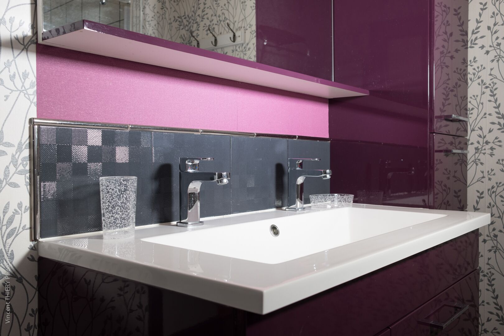 Ein modernes Badezimmer mit einem weißen Waschbecken, zwei Chromarmaturen und einer rosa Waschtischauflage.