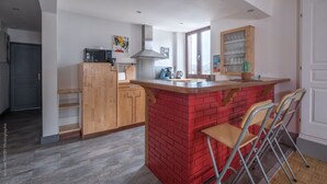 Een kleine keuken met een rode bakstenen eiland, houten kastjes en een magnetron.