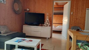 A cozy room with a TV on a cabinet, a sofa, a small table with magazines, and a bed with a wooden headboard. - Rent cosy apartment in the heart of Lioran resort close to the slopes (Laveissière)