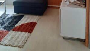 A cozy living room with wooden paneling, a round mirror, a small white cabinet, and a colorful rug. - Rent cosy apartment in the heart of Lioran resort close to the slopes (Laveissière)