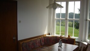 A dining area with a wooden table, bench seating, and a view of a green landscape through large windows.