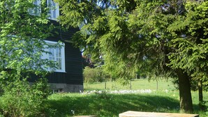 A rustic wooden bench in a grassy area with a house in the background.