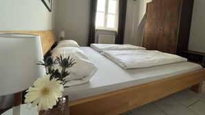 A bedroom with a bed, a wooden wardrobe, a window with curtains, a radiator, and a hanging light fixture. - Idyllic natural oasis - pure tranquillity just 5 minutes' walk from the Müritz  (Ludorf)