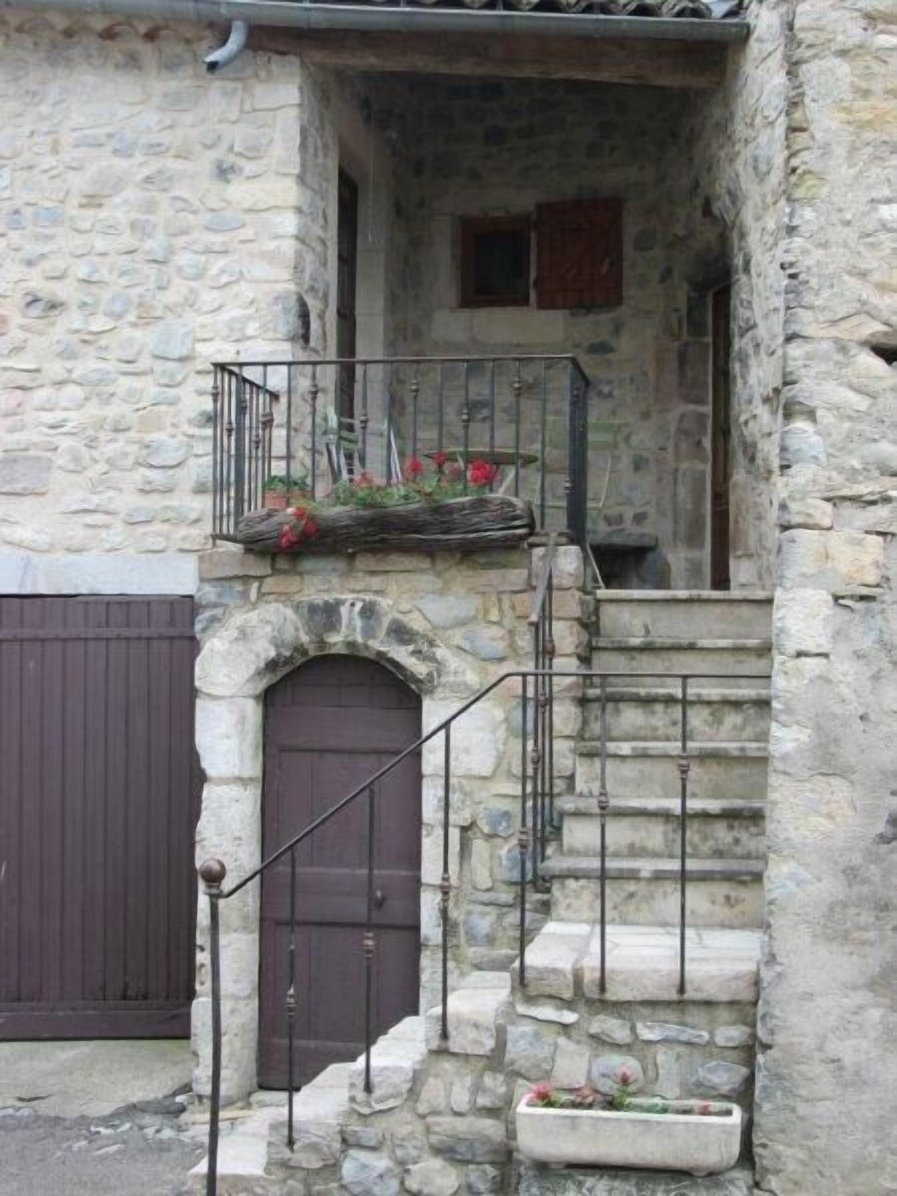 A stone building with a wooden door and a small balcony with a railing.