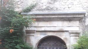 A stone building with a large wooden door, a stone staircase, and a small window with a metal grille. - Cozy cottage in the village of 4 Tours (Valvignères)