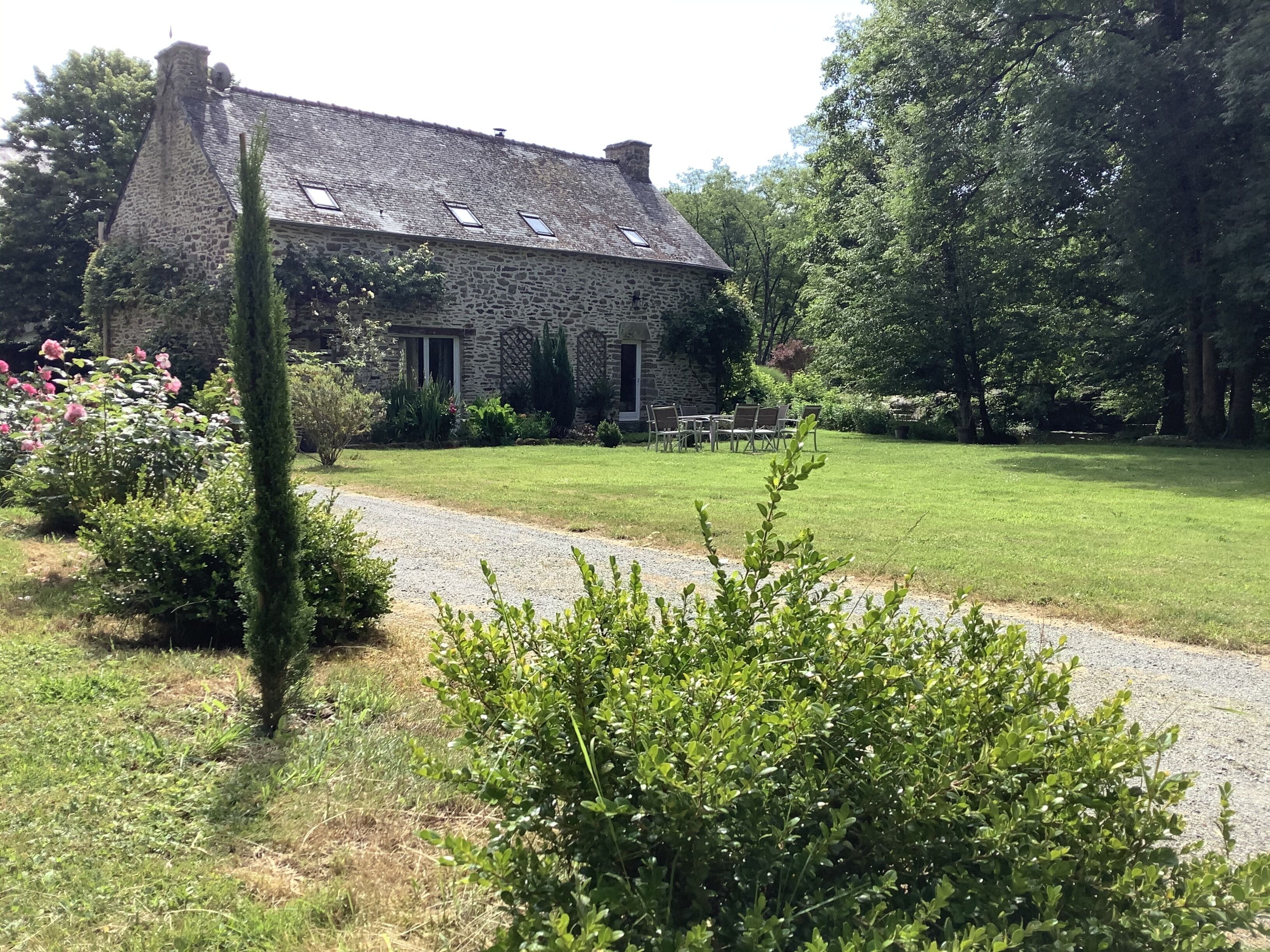 Une maison en pierre avec un chemin de gravier menant à une table et à des chaises en bois dans le jardin.