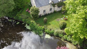 A stone house with a pond in front, surrounded by lush greenery. - Cottage ford of thorn (Peillac)