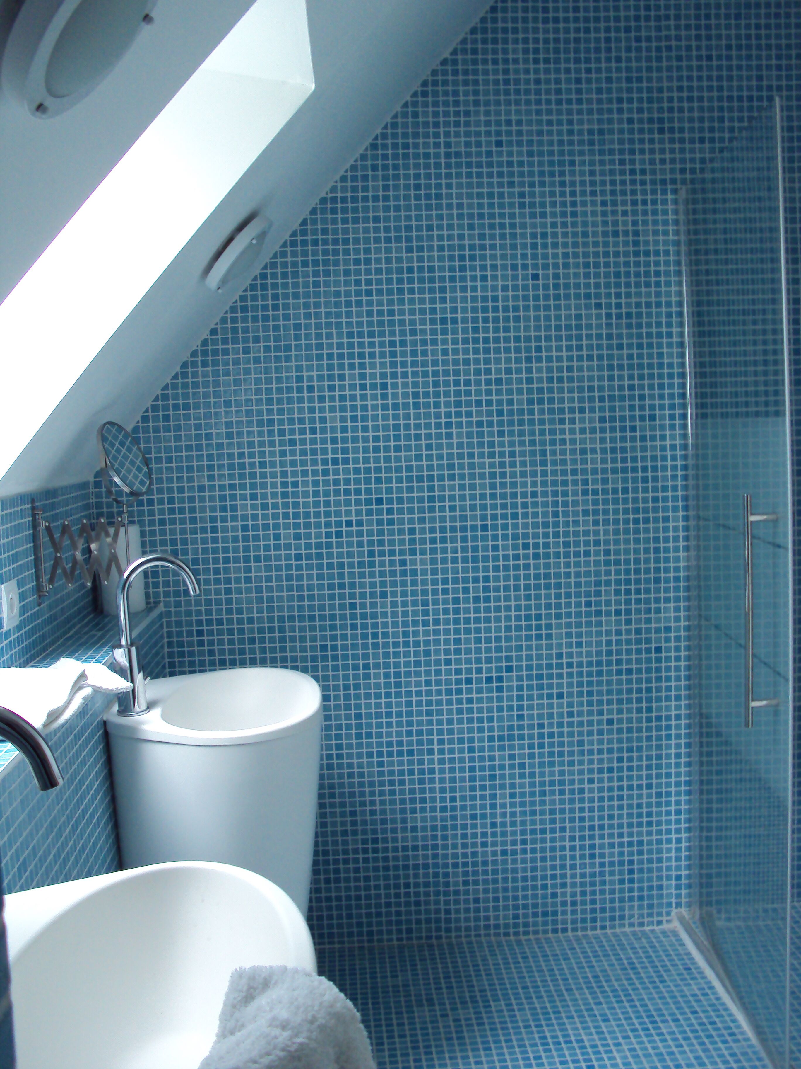 A bathroom with a white sink, a mirror, and a shower area with blue tiles.