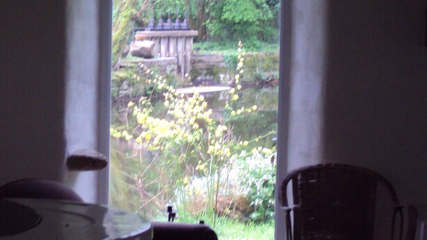 A room with a view through a window to a garden with a bench and a statue. - Cottage ford of thorn (Peillac)