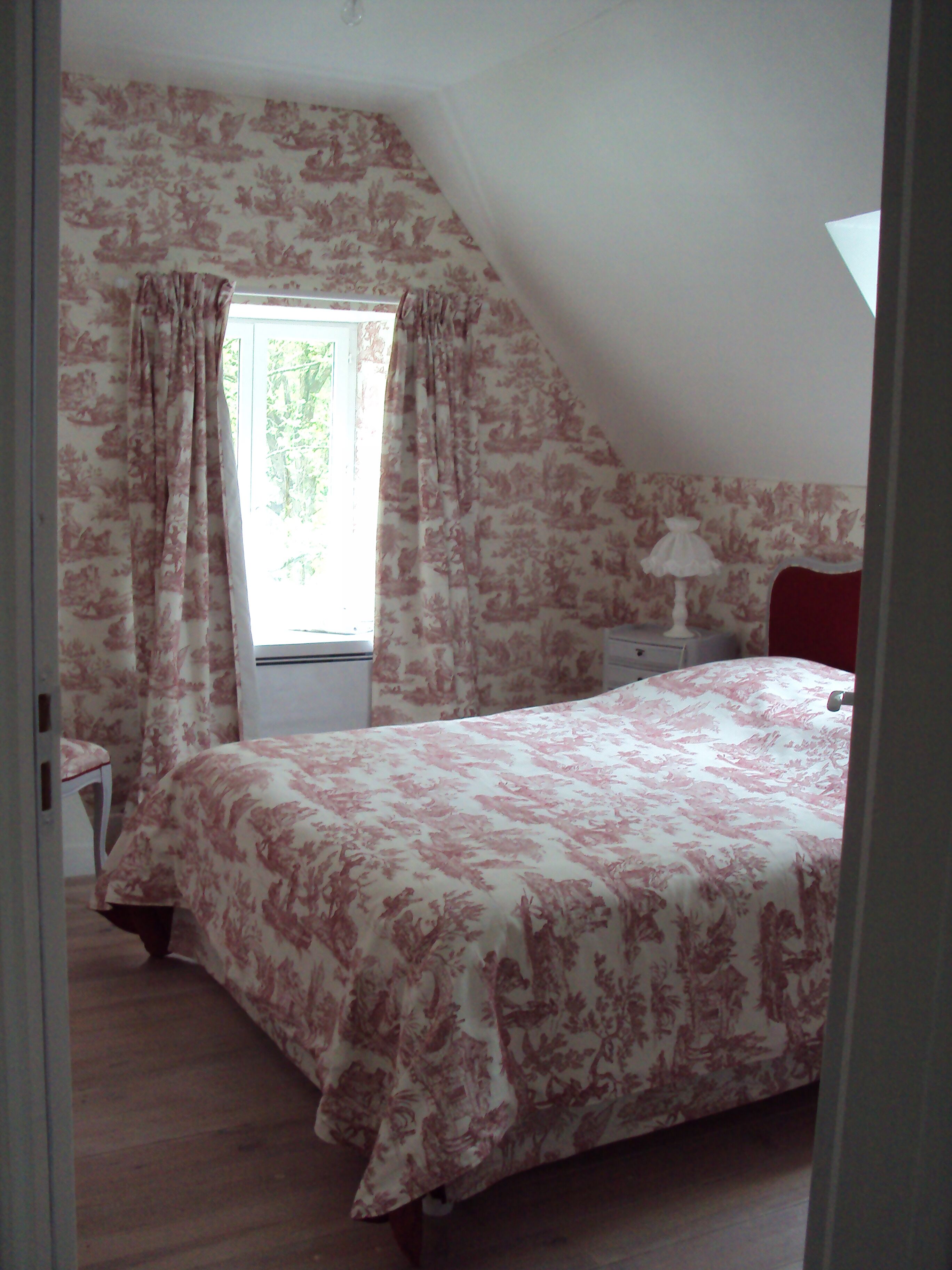 A bedroom with a bed, a nightstand, a lamp, and a window with curtains.