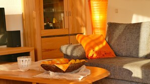 Una sala de estar acogedora con un aparador de madera, un televisor, una cesta de fruta y una lámpara anaranjada alta.