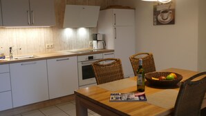 Una cocina con armarios blancos, una encimera de madera, una cafetera y una mesa de comedor con sillas.