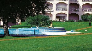 A swimming pool with steps, a person sitting on the steps, and a building with multiple balconies in the background.