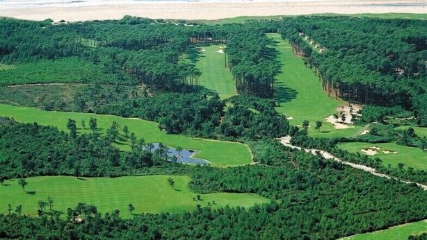 A golf course with multiple holes, surrounded by dense forests and a beach in the background.