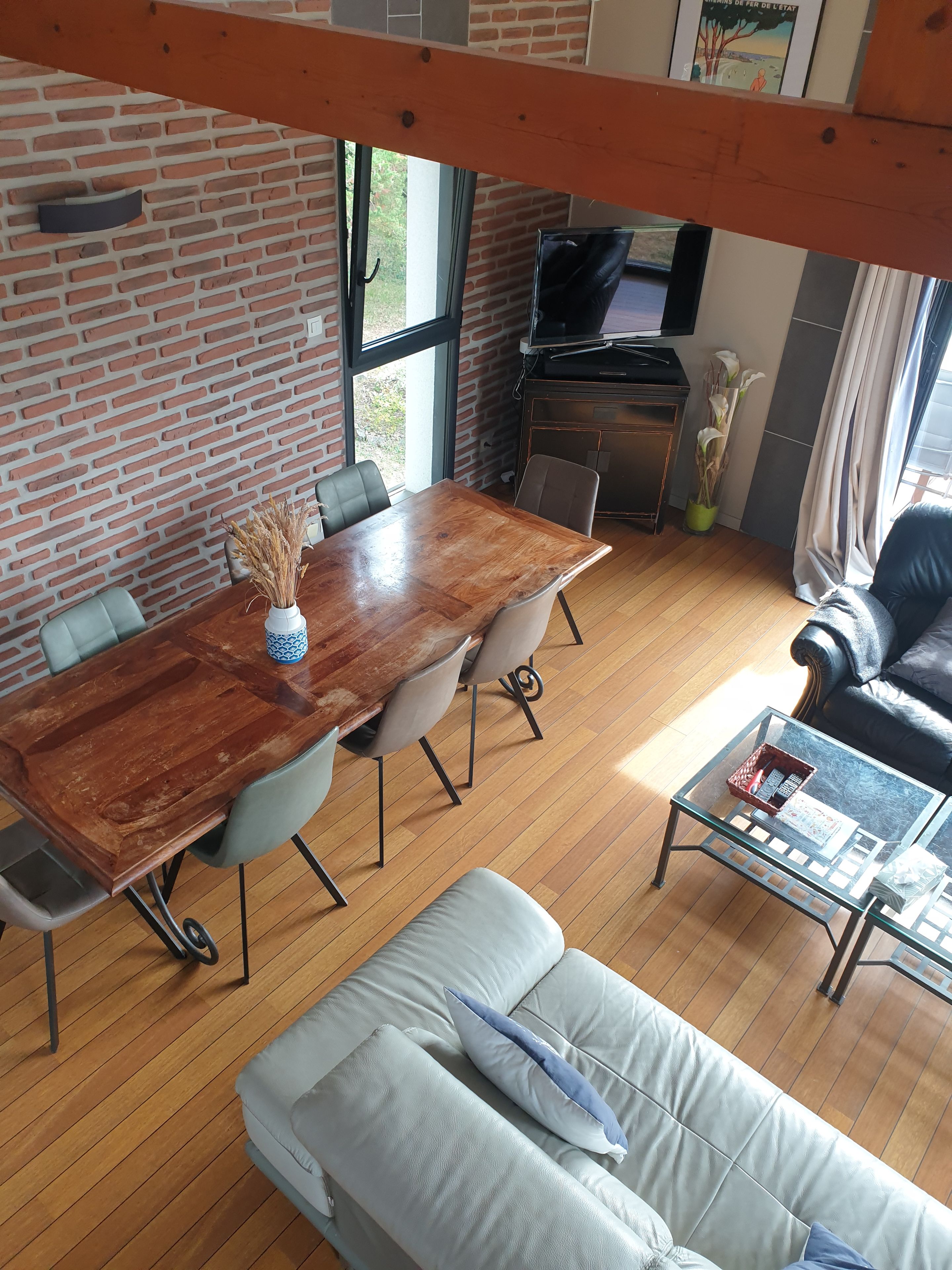Een eethoek met een houten tafel en stoelen, een bank, een glazen salontafel en een televisie op de achtergrond.