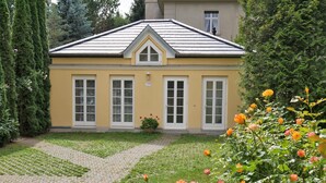 A yellow building with a tiled roof, three windows, and a paved pathway leading to it.