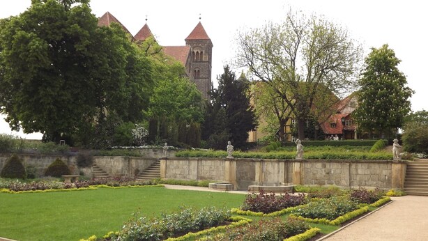 A formal garden with manicured lawns, stone pathways, and statues.
