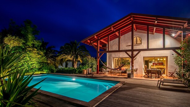 A modern house with a pool, surrounded by lush greenery and palm trees.