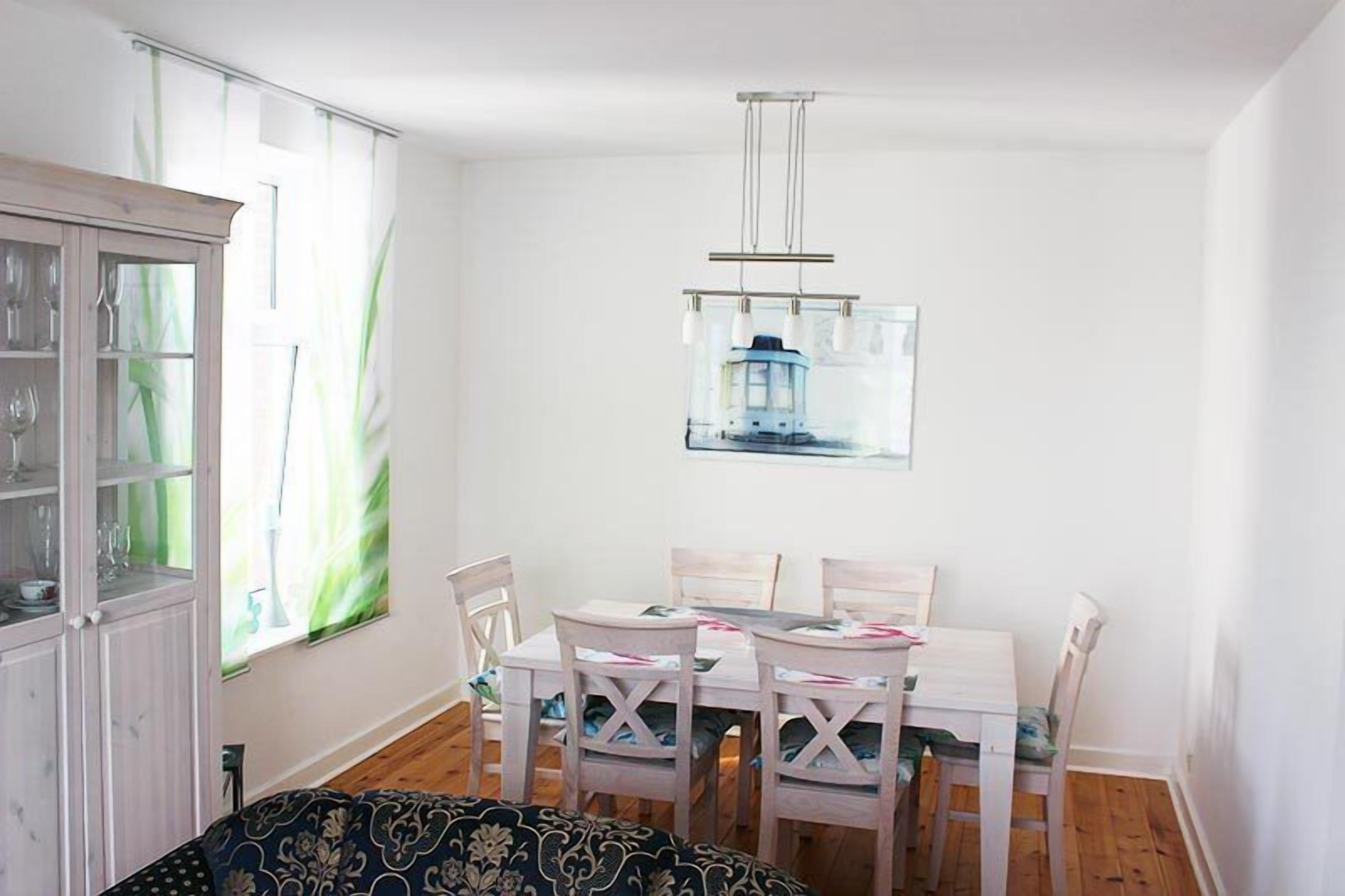 A dining area with a white table and chairs, a cabinet with glass doors, and a window with a view of a building.