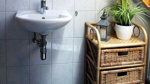Een badkamer met een wit wastafelmeubel, een spiegel en een plant in een pot.