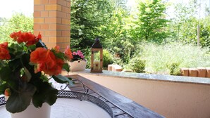 Een terras met een bakstenen pilaar, een potplant met rode bloemen, een lantaarn en een tafel met decoratieve rand.