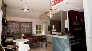 Una cocina moderna con una isla central, vigas de madera y un comedor con una mesa y sillas blancas.