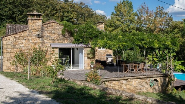 Una casa de piedra con terraza de madera y piscina.
