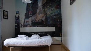 Un dormitorio con una cama, una lámpara negra y un mural de paisaje urbano en la pared.