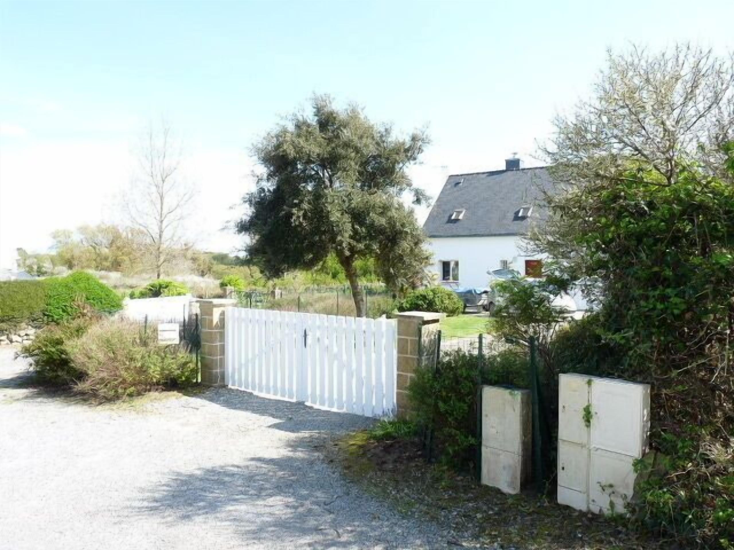 A gated property with a gravel driveway leading to a white house with a grey roof.