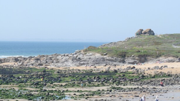 Un paysage côtier caractérisé par un terrain rocheux, une plage de sable et une vue dégagée sur l’océan.