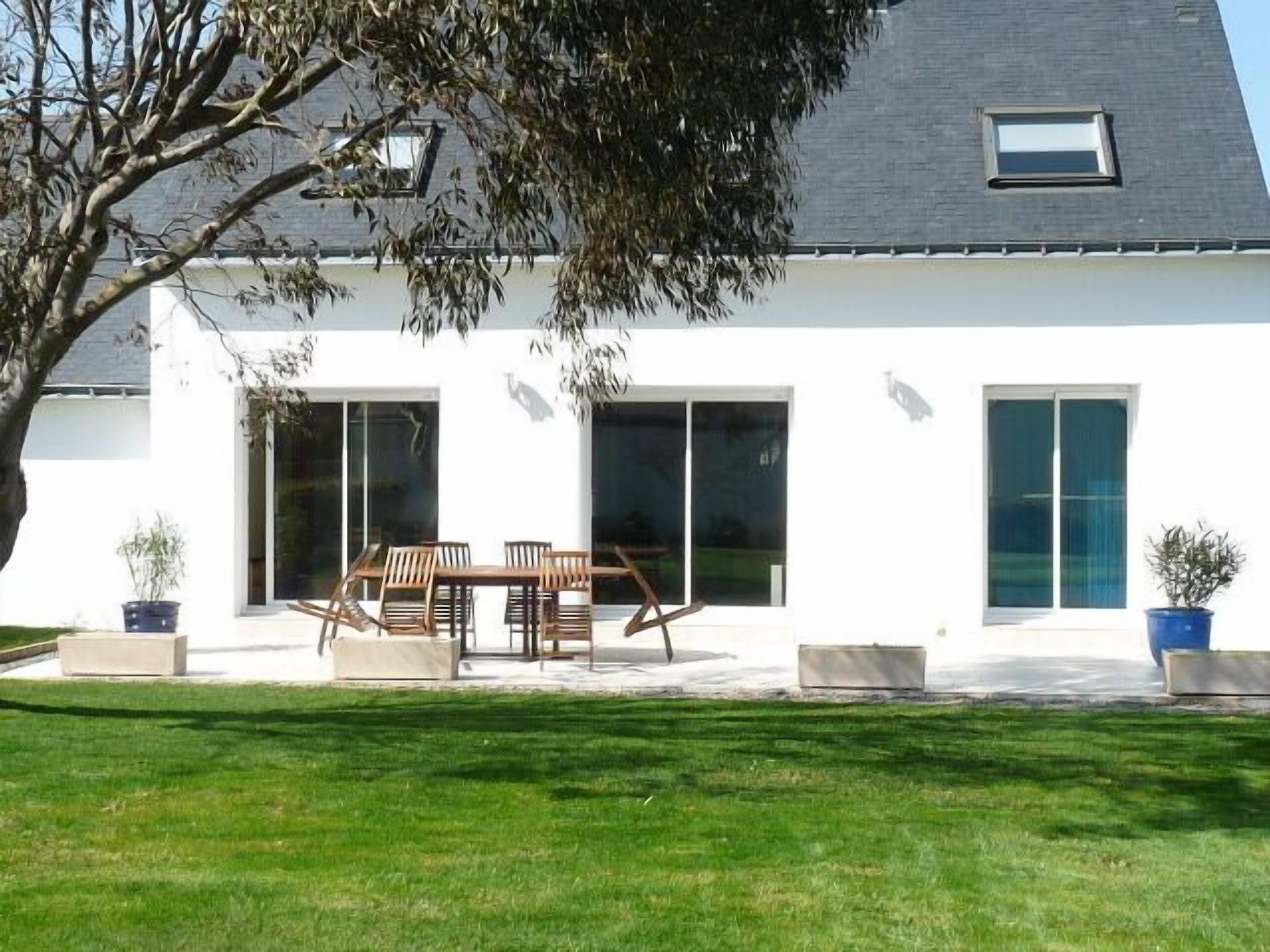 A modern white house with a patio, a dining table, and chairs.