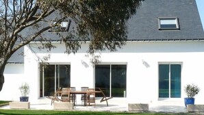 Une maison moderne, blanche, dotée d’un patio, d’une table à manger et de chaises.