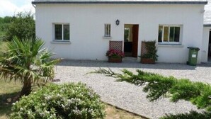 Ein weißes, zweistöckiges Haus mit einem Schotterweg, einem kleinen Garten mit Pflanzen und Blumen sowie einer Tür zum Eingang.